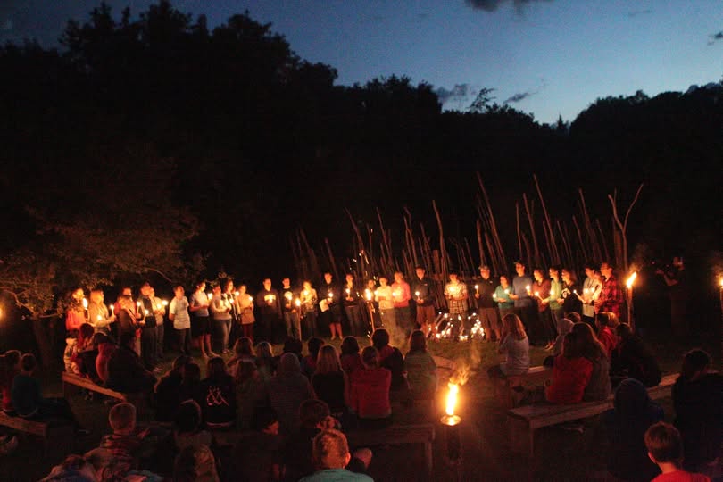 Scene at dusk of candlelight ceremony with many candles lit being held by campers.